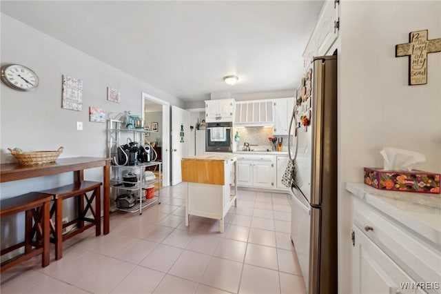 kitchen with light tile patterned floors, butcher block counters, backsplash, appliances with stainless steel finishes, and white cabinetry