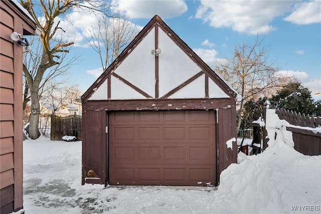 snow covered garage with a detached garage and fence