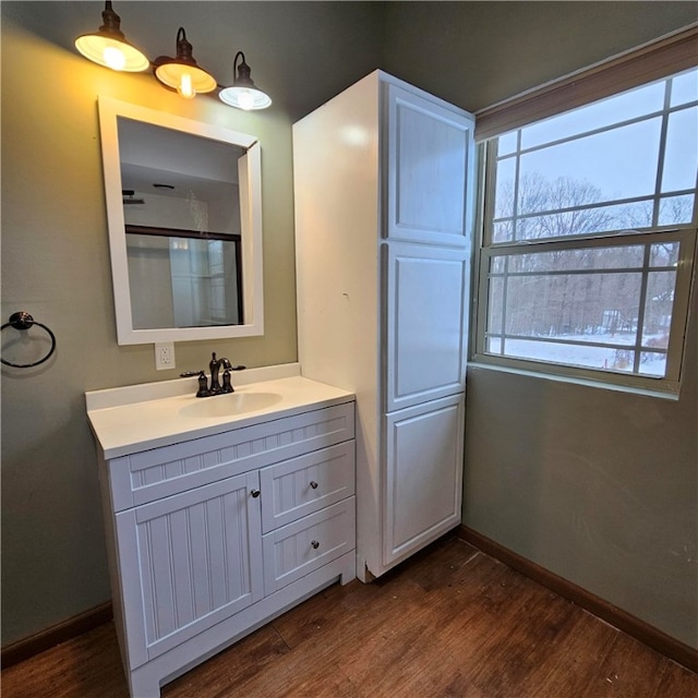 full bath with a shower with shower door, vanity, baseboards, and wood finished floors