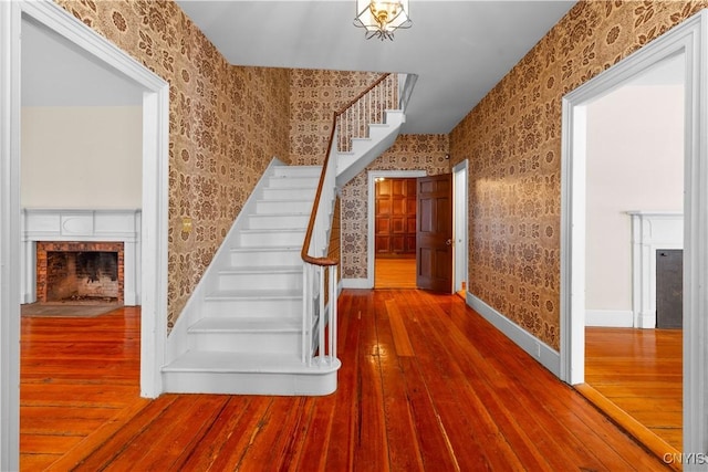 stairway with wood finished floors, a brick fireplace, baseboards, and wallpapered walls