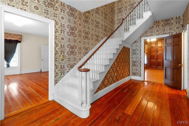 stairway featuring baseboards, wood finished floors, and wallpapered walls