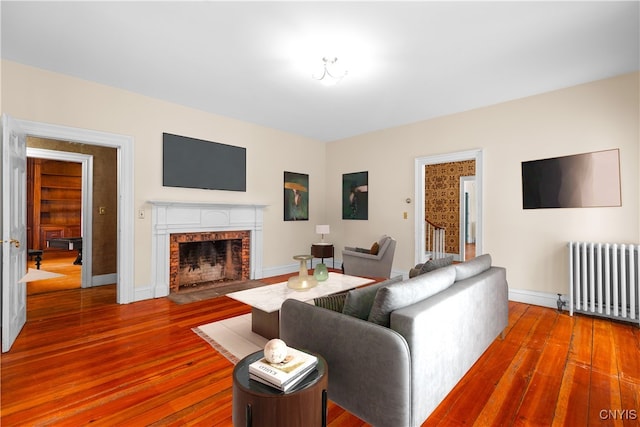 living room with a fireplace with flush hearth, baseboards, radiator heating unit, and wood finished floors