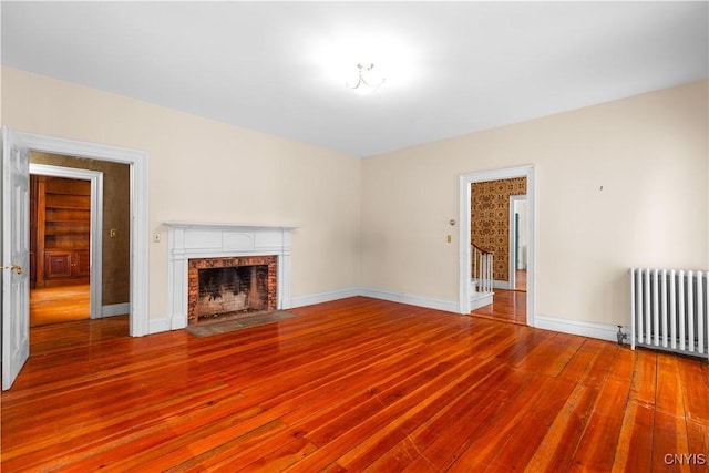 unfurnished living room with a brick fireplace, radiator, baseboards, and wood finished floors