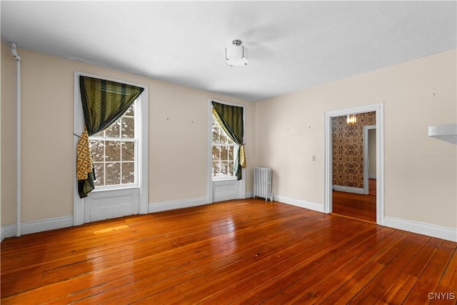 spare room with baseboards, wood finished floors, and radiator