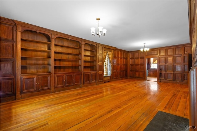 interior space featuring light wood finished floors, built in features, a notable chandelier, and wood walls