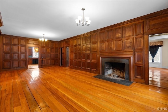 unfurnished living room with an inviting chandelier, a fireplace with flush hearth, light wood-style floors, and wood walls