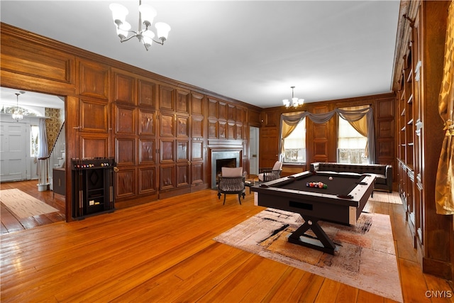 game room with a fireplace, pool table, a decorative wall, an inviting chandelier, and light wood-style floors