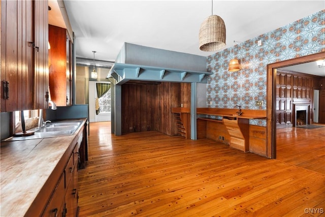 kitchen with wallpapered walls, a fireplace, wood finished floors, and decorative light fixtures