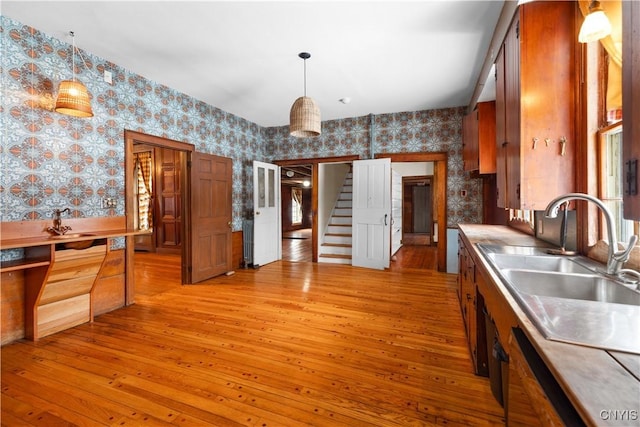 kitchen with light wood-type flooring, wallpapered walls, a sink, and hanging light fixtures