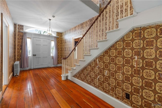 foyer entrance with radiator, stairway, wood finished floors, baseboards, and wallpapered walls