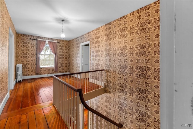 corridor with radiator, wallpapered walls, baseboards, and wood finished floors