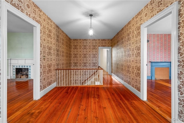 unfurnished room with a high end fireplace, wallpapered walls, baseboards, and wood finished floors