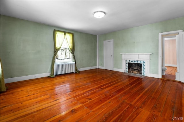 unfurnished living room with baseboards, a fireplace, radiator heating unit, and wood finished floors