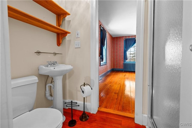 bathroom with wallpapered walls, baseboards, radiator, toilet, and wood finished floors