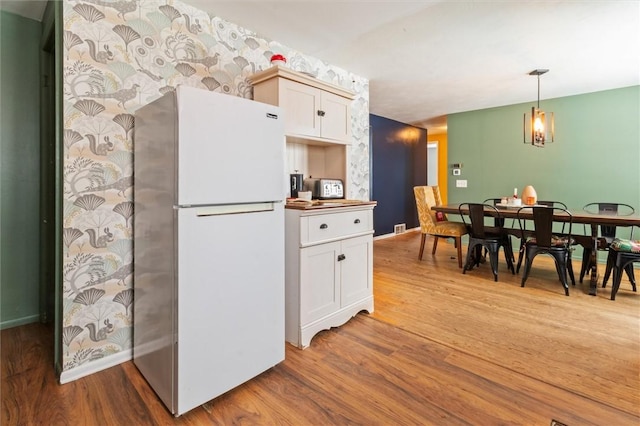 kitchen featuring hanging light fixtures, light wood-style flooring, white cabinetry, and freestanding refrigerator