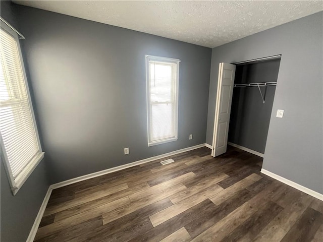 unfurnished bedroom with a closet, visible vents, dark wood-type flooring, a textured ceiling, and baseboards