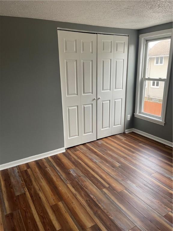 unfurnished bedroom featuring dark wood-style floors, a closet, a textured ceiling, and baseboards