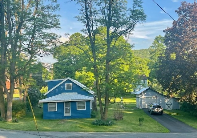 bungalow with a detached garage, metal roof, aphalt driveway, an outbuilding, and a front lawn