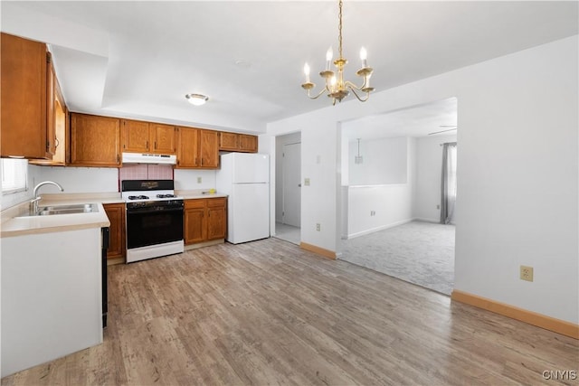 kitchen with under cabinet range hood, a sink, light countertops, range, and freestanding refrigerator