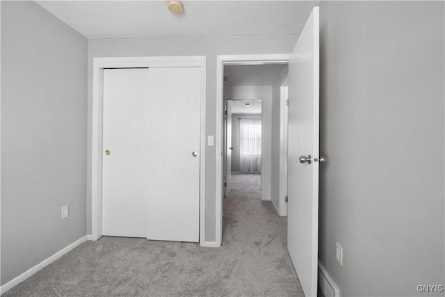 unfurnished bedroom with baseboards, a closet, and light colored carpet