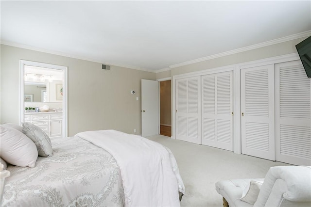 bedroom featuring ensuite bathroom, light carpet, visible vents, multiple closets, and ornamental molding