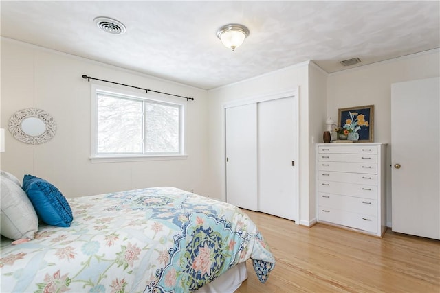 bedroom with light wood finished floors, visible vents, a closet, and ornamental molding