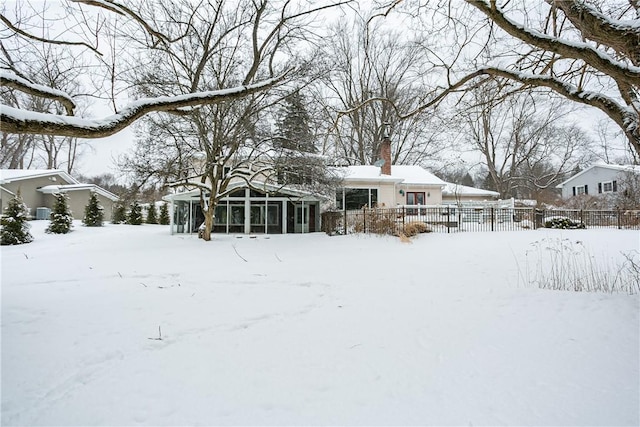 snow covered back of property featuring a chimney, fence, and a sunroom