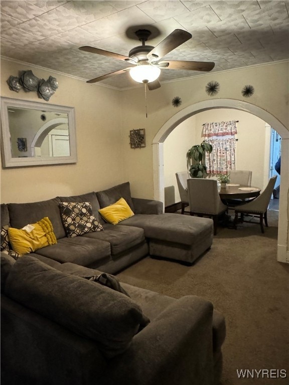 living area featuring arched walkways, ceiling fan, carpet, and crown molding