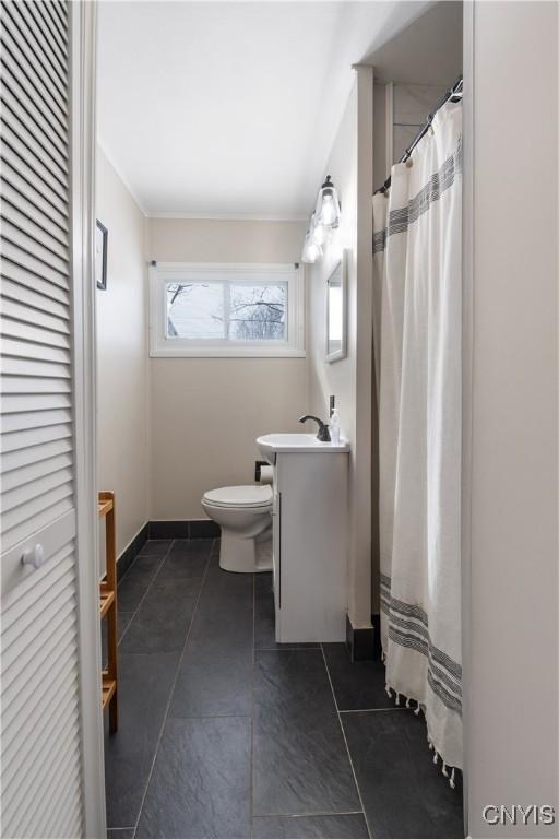 bathroom featuring toilet, vanity, baseboards, ornamental molding, and a closet