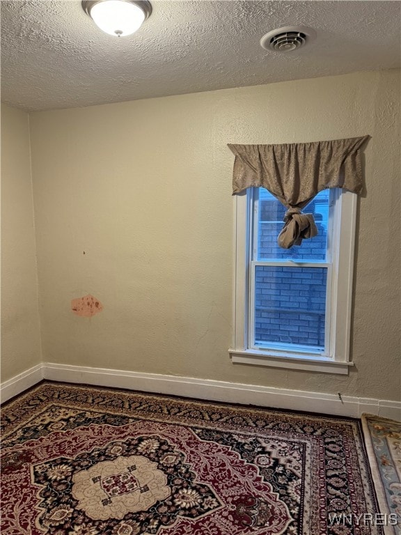 empty room with baseboards, visible vents, a textured ceiling, and a textured wall