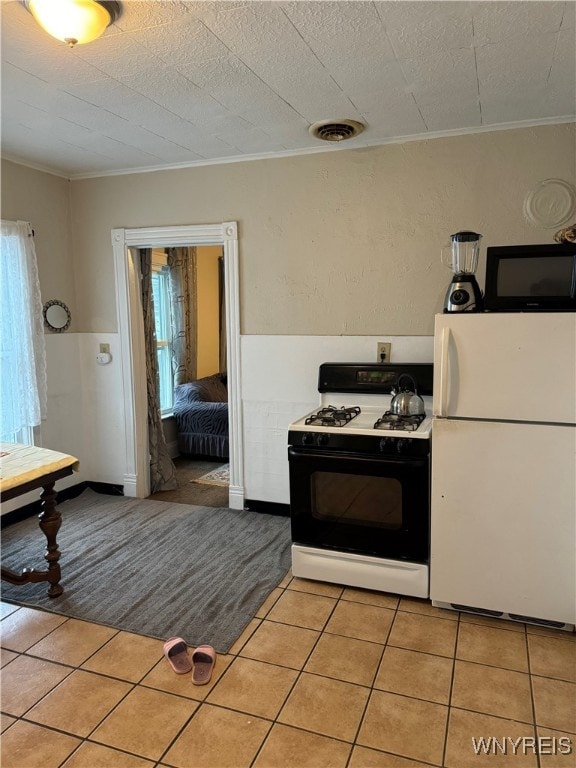 kitchen featuring light tile patterned floors, visible vents, ornamental molding, freestanding refrigerator, and gas range oven