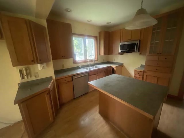 kitchen with stainless steel appliances, hanging light fixtures, light wood-style floors, a kitchen island, and a sink