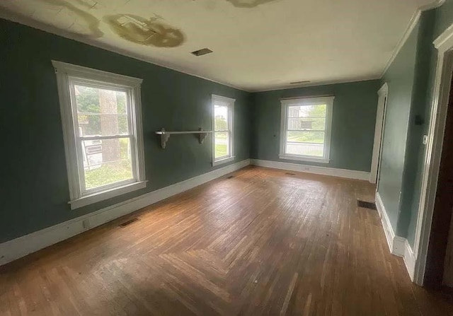 empty room with visible vents, baseboards, a wealth of natural light, and wood finished floors