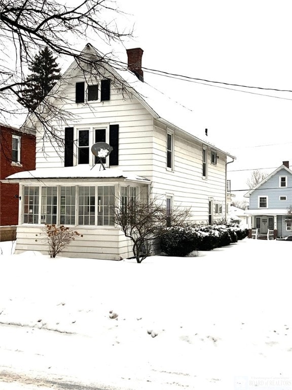 snow covered property featuring a chimney and a sunroom