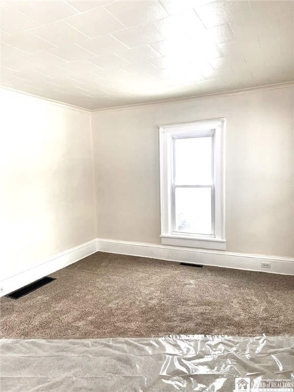 carpeted spare room with ornamental molding, visible vents, and baseboards