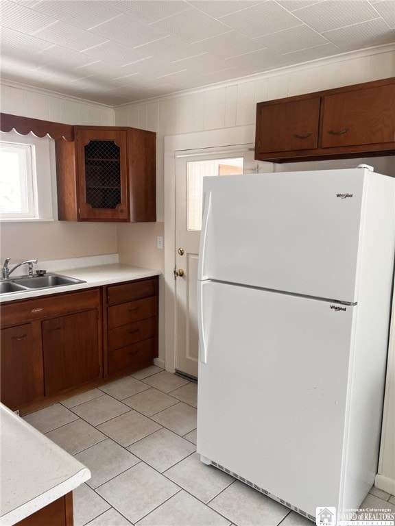 kitchen with light tile patterned floors, a sink, light countertops, ornamental molding, and freestanding refrigerator