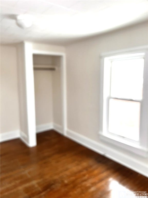 unfurnished bedroom with dark wood-style floors, a closet, and baseboards