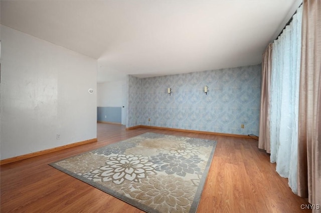 living room featuring wallpapered walls, baseboards, and wood finished floors