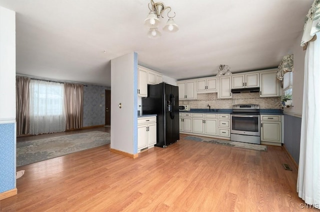 kitchen with stainless steel electric range oven, dark countertops, light wood-type flooring, under cabinet range hood, and black fridge