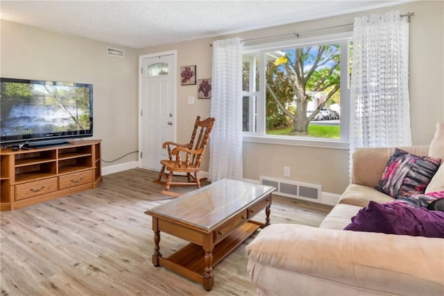 living area with light wood-type flooring, baseboards, visible vents, and a textured ceiling