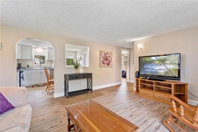 living area with arched walkways, a textured ceiling, baseboards, and light wood-style floors