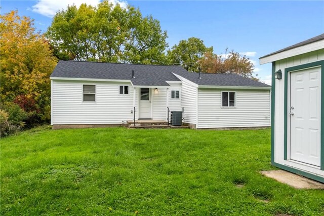 rear view of property with an outbuilding, roof with shingles, a lawn, and central AC unit