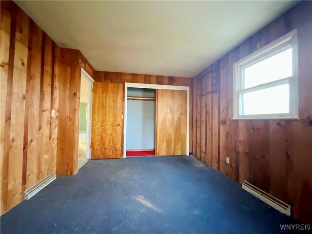 unfurnished bedroom featuring a baseboard heating unit, a closet, and wood walls