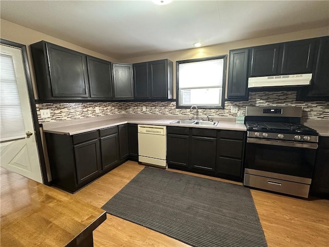 kitchen featuring stainless steel range with gas stovetop, white dishwasher, light countertops, under cabinet range hood, and a sink