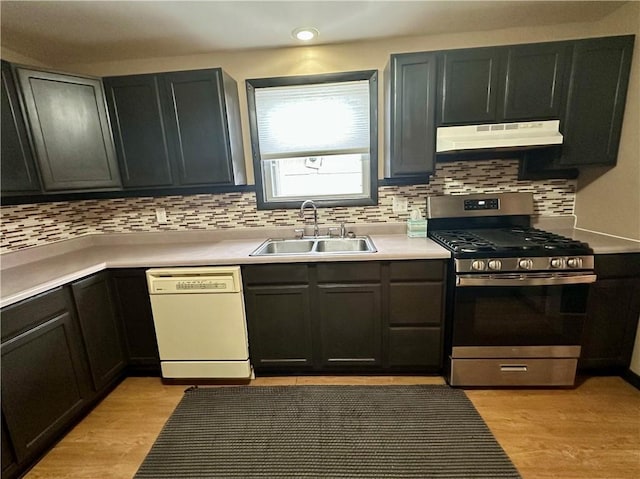 kitchen with white dishwasher, light countertops, under cabinet range hood, stainless steel range with gas cooktop, and a sink