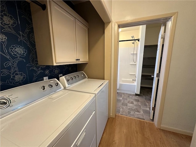 clothes washing area featuring light wood-type flooring, washing machine and dryer, cabinet space, and baseboards