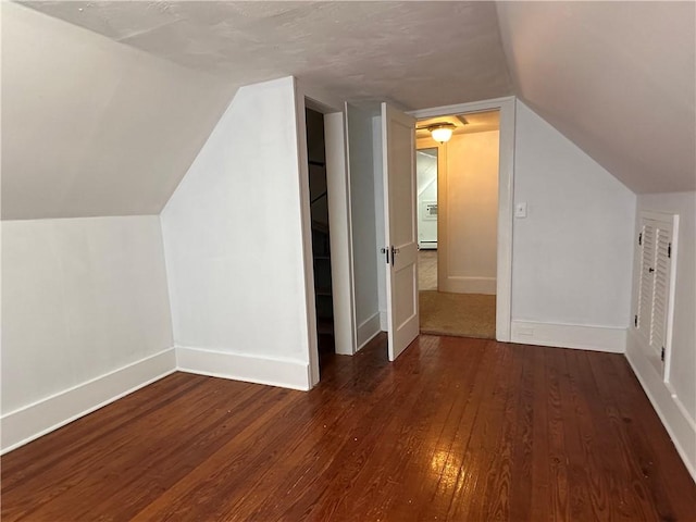 additional living space with baseboards, vaulted ceiling, and dark wood-type flooring