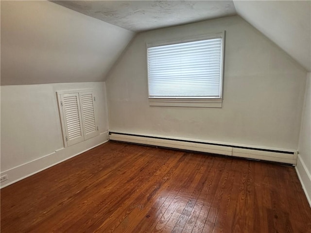 additional living space with a baseboard heating unit, vaulted ceiling, dark wood finished floors, and baseboards