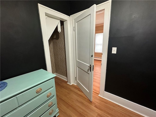 hall featuring a baseboard radiator, baseboards, and wood finished floors