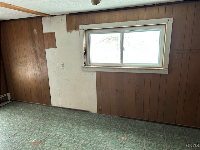 spare room with wood walls, dark floors, baseboard heating, and a textured ceiling